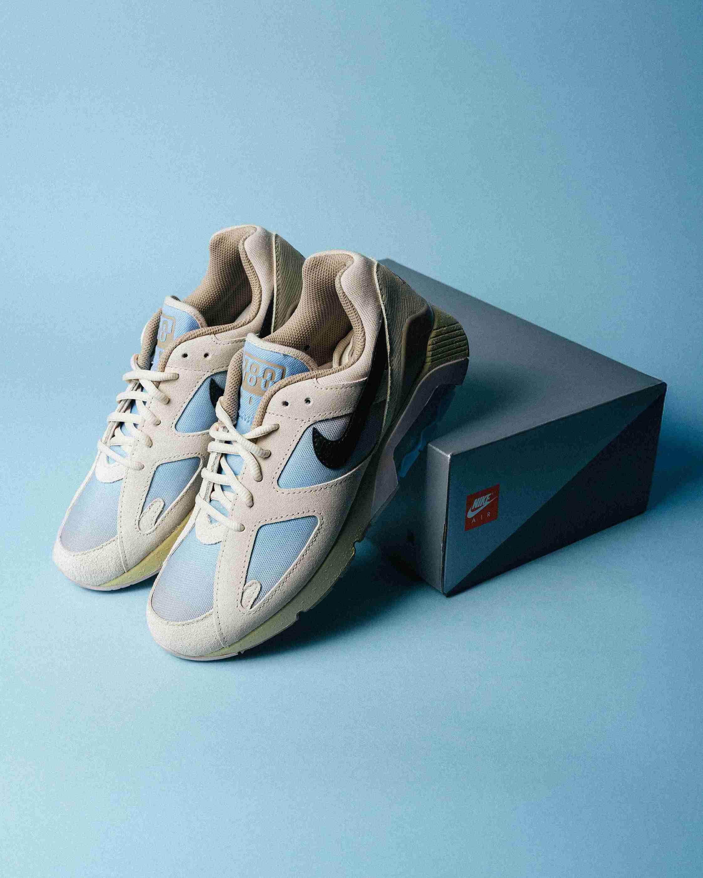 Paire de sneakers beige et bleu clair posée sur un fond bleu, vue de trois quarts avec mise en avant des formes et détails du modèle.
